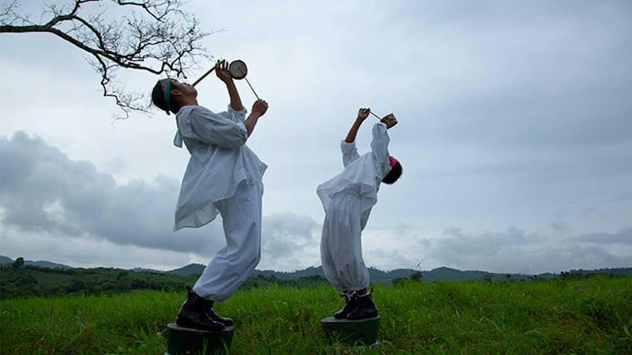 Danzante volador adulto y niño de Papantla ejecutando la música ritual - hombre tocando tambor tradicional y niño soplando flauta de carrizo durante la ceremonia de los Voladores de Papantla al aire libre.