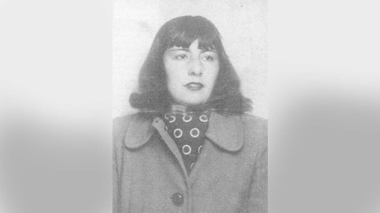 Fotografía en blanco y negro de María Luisa Bombal, tomada de su pasaporte. Ella es una mujer joven con cabello oscuro hasta los hombros, peinado en un bob con flequillo. Mira directamente a la cámara con una expresión seria. Viste un abrigo oscuro con solapas anchas y debajo, un pañuelo de cuello con un patrón de lunares o círculos blancos. La foto tiene un aspecto vintage y está enmarcada por bordes grises y borrosos.